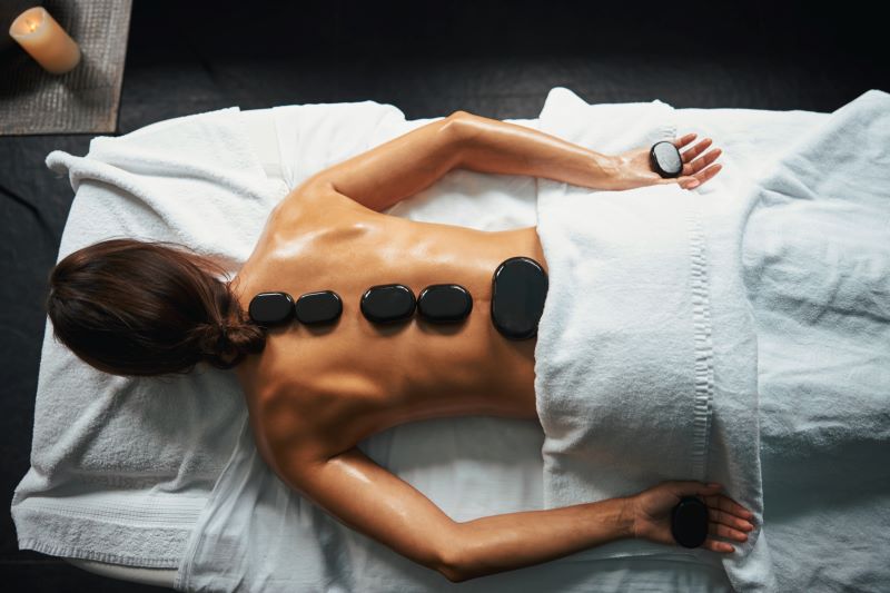 A woman with hot stone on her back with a calm ambiance on a spa.